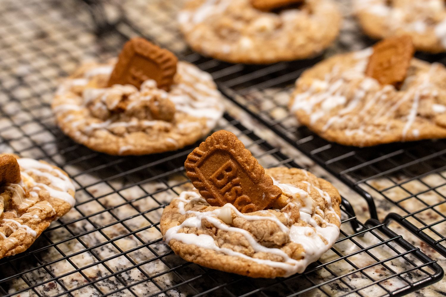 Cookie butter cookies on a cooling rack, each topped with a speculoos cookie and white drizzle