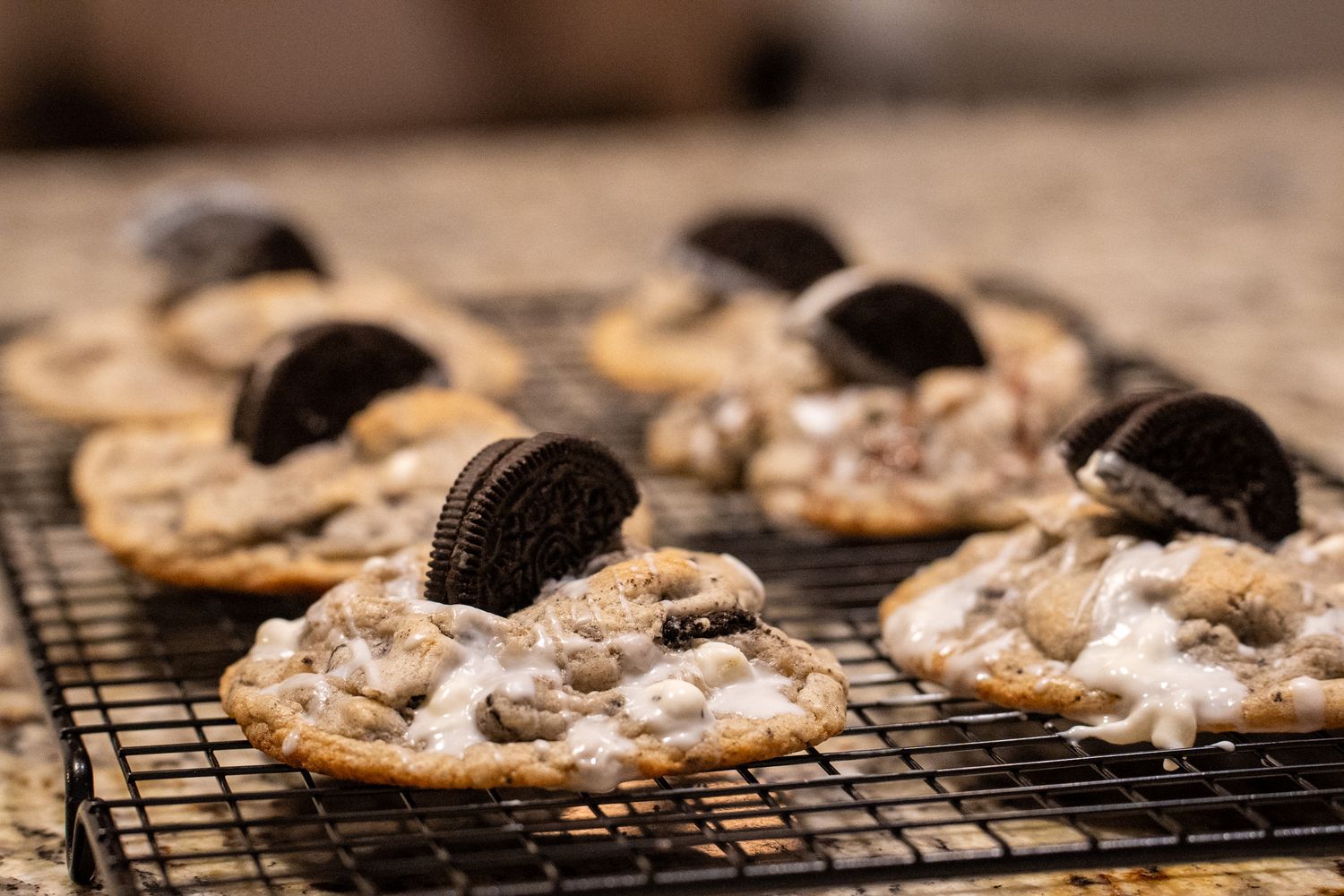 A cooling rack of cookies and cream cookies with white icing and halved sandwich cookies